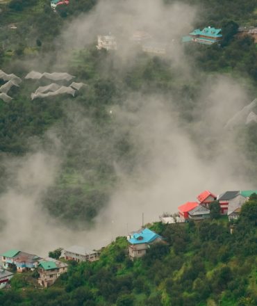Scenic aerial view of a mist-covered village nestled in Himachal Pradesh, India, surrounded by lush greenery.