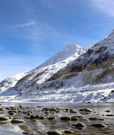 Discover the serene beauty of snow-capped mountains and a tranquil river in Manali, India.