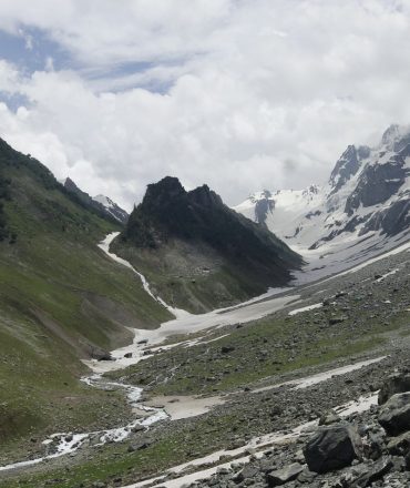 Stunning mountain landscape with snow-capped peaks, a river, and lush greenery.
