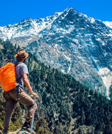 Man exploring breathtaking mountain scenery with snow-capped peaks under a clear blue sky.