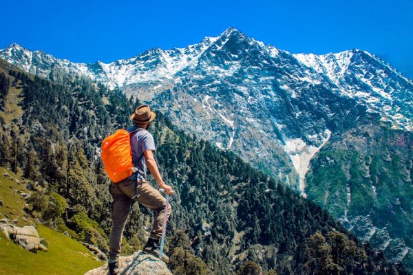 Man exploring breathtaking mountain scenery with snow-capped peaks under a clear blue sky.