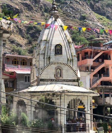 A picturesque Hindu temple surrounded by colorful flags in a mountainous region.