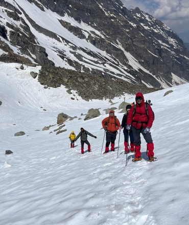 Adventurers trekking through snow in Hampta Pass, Himalayas. Experience majestic alpine scenery.