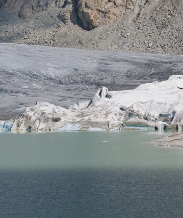 Breathtaking view of a Swiss glacier surrounded by mountains and a serene blue lake, capturing nature's raw beauty.
