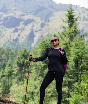 Woman hiking with trekking pole in a lush mountain forest, exuding confidence and adventure.