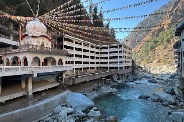 Colorful flags draped over Manikaran temple by a rushing river in Himachal Pradesh, India.