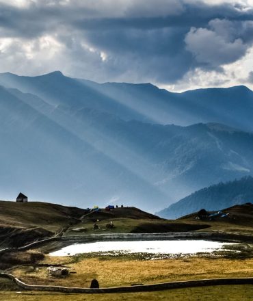 A breathtaking view of mountains under a dramatic sky with sun rays illuminating the landscape.