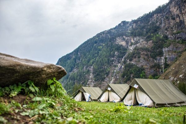 Row of tents on a grassy field by a mountain backdrop, perfect for outdoor adventure.